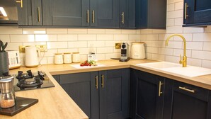 A modern kitchen with dark cabinetry, a wooden countertop, a gas stove, a coffee maker, and a gold faucet.