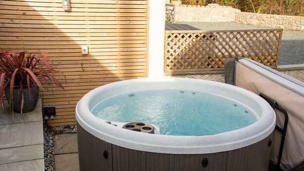 A hot tub in an outdoor setting with a wooden deck, a potted plant, and a lattice fence in the background.