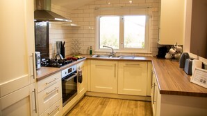 Een moderne keuken met witte kasten, een houten aanrecht, een inbouwoven, een fornuis en een raam voor natuurlijk licht.