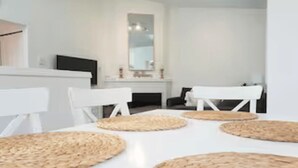 A modern, minimalist room with a white table, woven placemats, and a flat-screen TV on a white console.