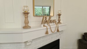 A fireplace mantel with a mirror above it, flanked by two candle holders and a wooden sign with beads.