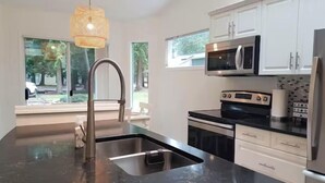 A modern kitchen with a black marble countertop, stainless steel appliances, white cabinets, and a large window providing a view of the outdoors.