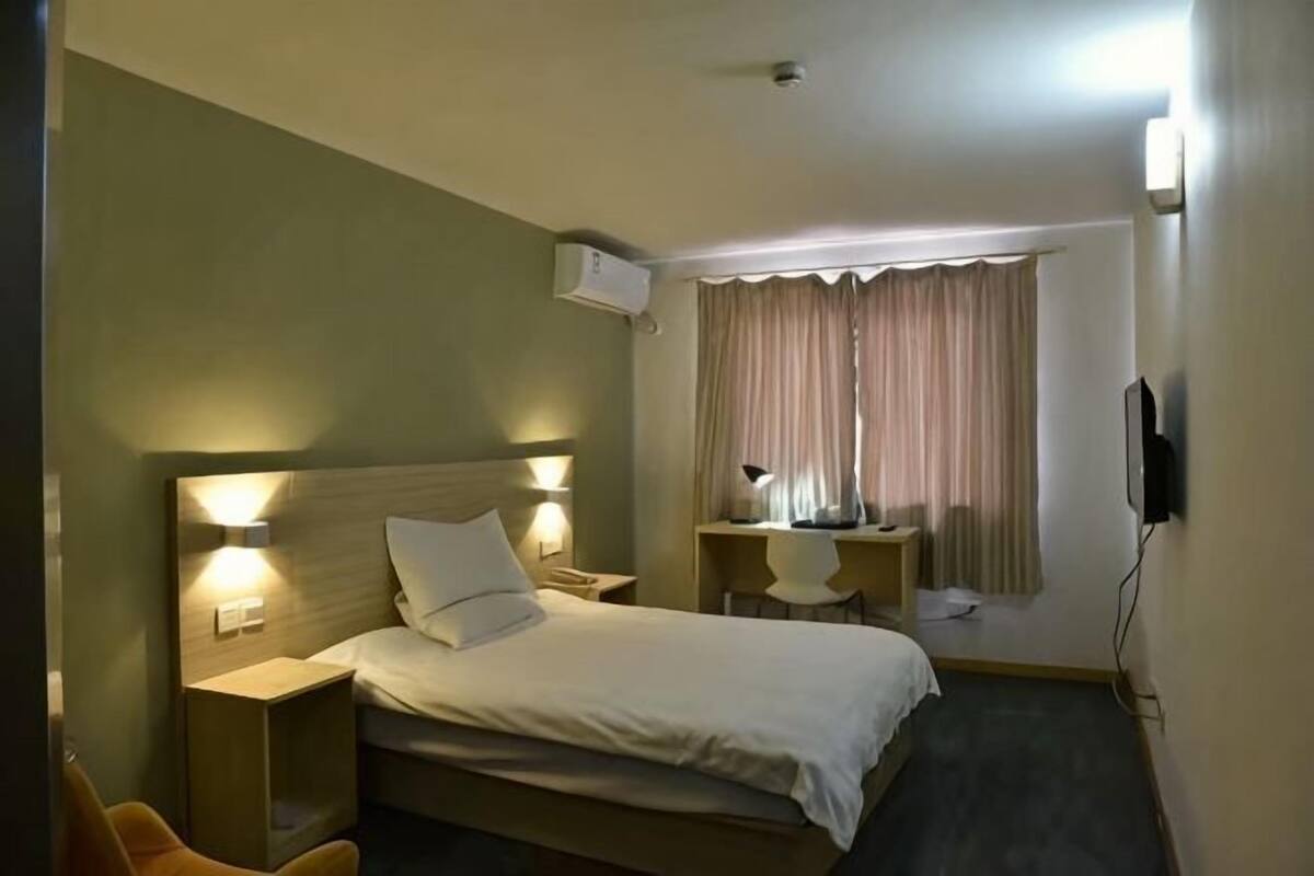 Habitación de hotel con cama, lámparas de noche, escritorio con silla, televisión y ventana con cortinas.