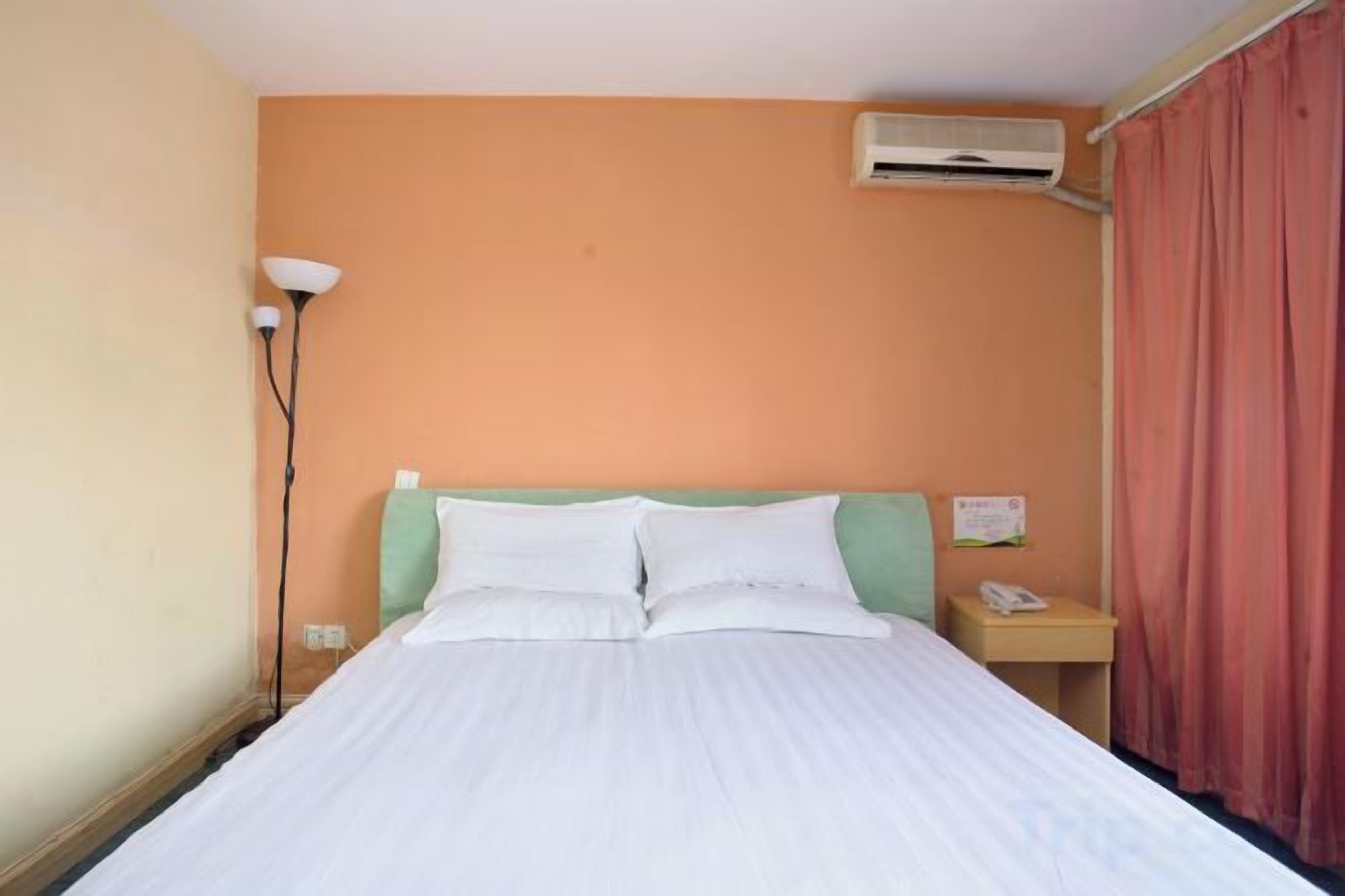 Een hotelkamer met een bed, een nachtkastje, een lamp en een rood gordijn.