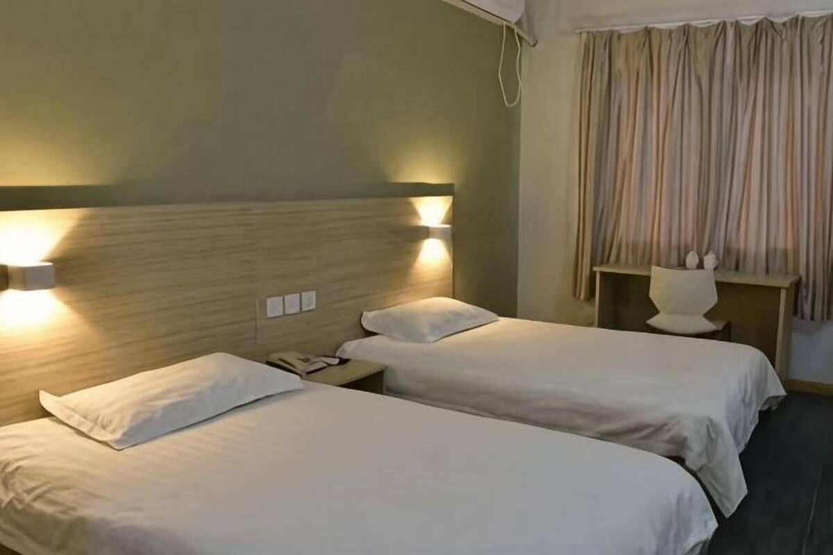 Una habitación de hotel con dos camas, lámparas de noche, mesitas de noche y una cortina.
