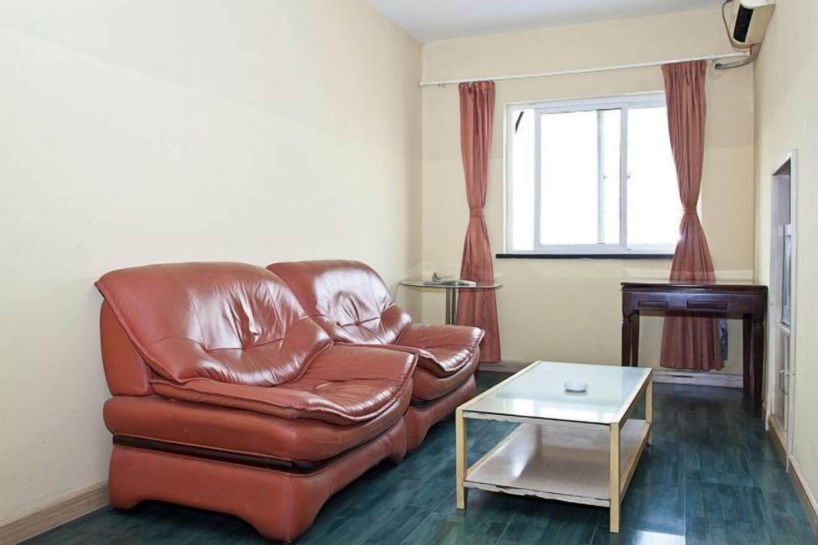 Una habitación con sofá de cuero, una mesita y una ventana con cortinas.