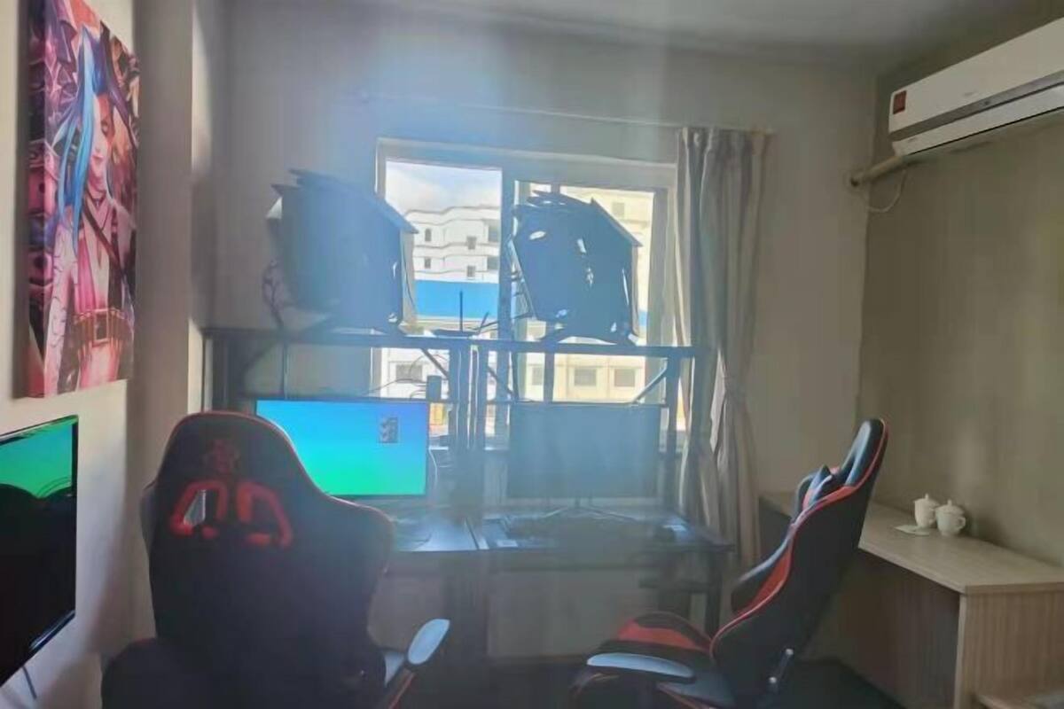 Una habitación con escritorio, dos sillas gamer, televisor y ventana con vista a edificios.