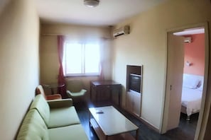 Un espacio habitable compacto con sofá, una mesita, televisión y cama en una habitación contigua.