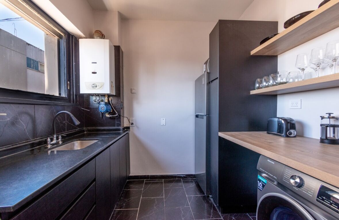 Una cocina compacta con lavadora integrada, un refrigerador y un ventanal sobre el fregadero.