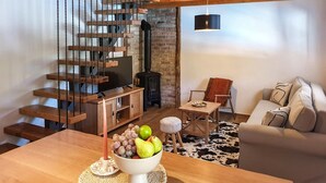 A modern living room with a wooden staircase, a black wood-burning stove, a sofa, a dining table with fruit, and a cowhide rug. - Amazing home in Druzilovec with sauna (Druzilovec)