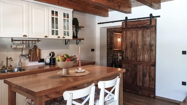A kitchen with white cabinets, a wooden island with a bowl of fruit, and a rustic wooden door. - Amazing home in Druzilovec with sauna (Druzilovec)