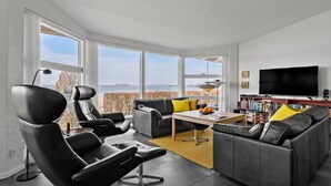 A modern living room with a large window, a flat-screen TV, and a bookshelf. - 3 bedroom gorgeous home in Hejls (Hejls)