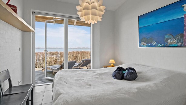 A bedroom with a large bed, a view of a beach, a modern pendant light, and a painting on the wall. - 3 bedroom gorgeous home in Hejls (Hejls)