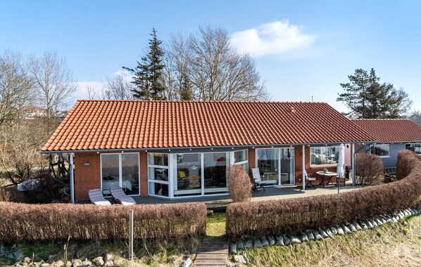 A modern house with a red-tiled roof, large glass windows, and a wooden deck.