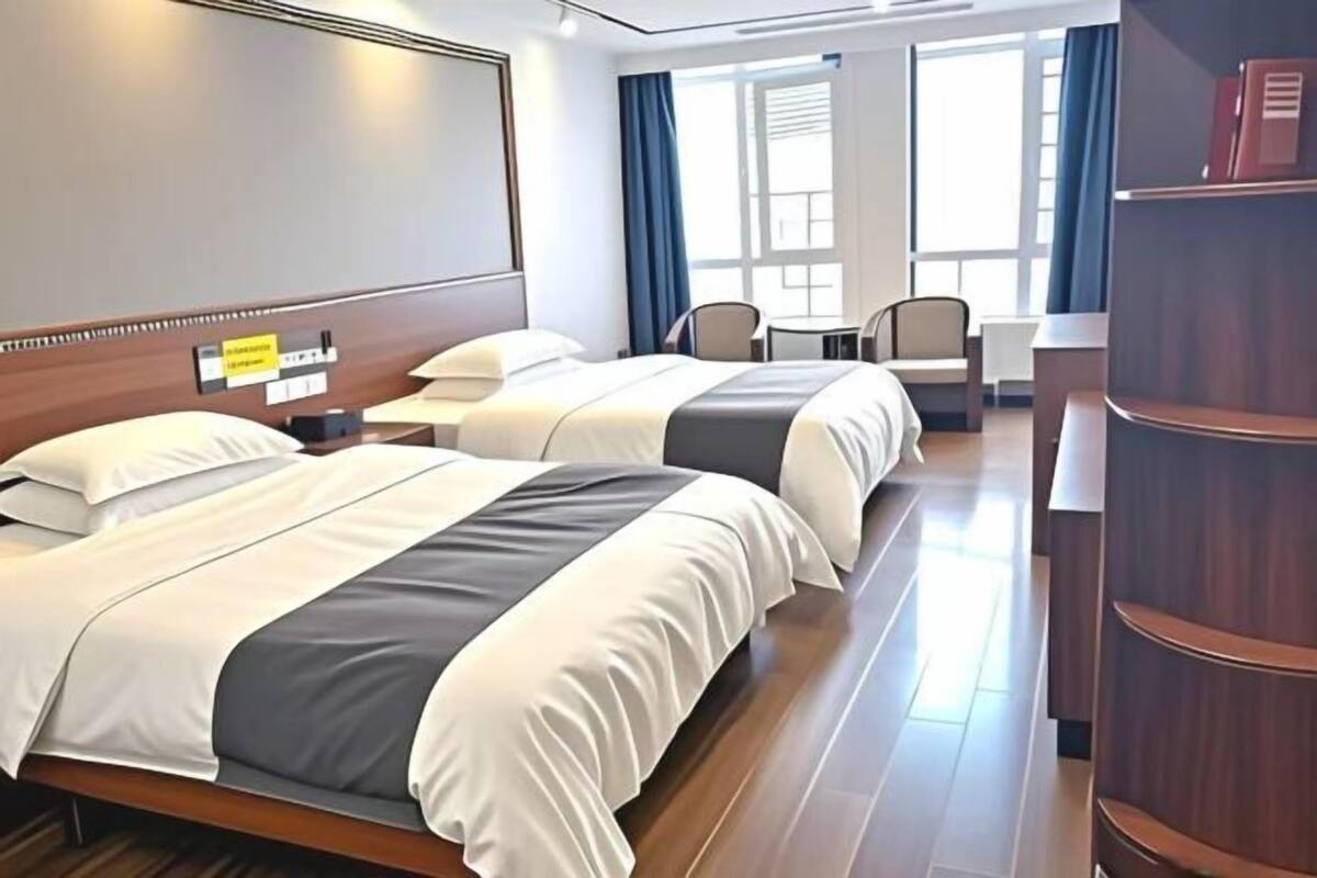 Habitación de hotel con dos camas, un escritorio, una silla y una estantería.