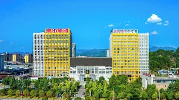 A large hotel with multiple floors, a prominent entrance, and a surrounding green area with trees.