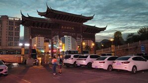A traditional Chinese gate with a modern parking lot in the foreground.