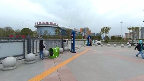 A public space with a curved building, a pedestrian walkway, bollards, and a few people.