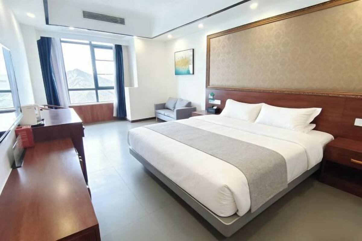 Habitación de hotel con una cama grande, un escritorio, una silla, una mesita de noche y una ventana con cortinas.
