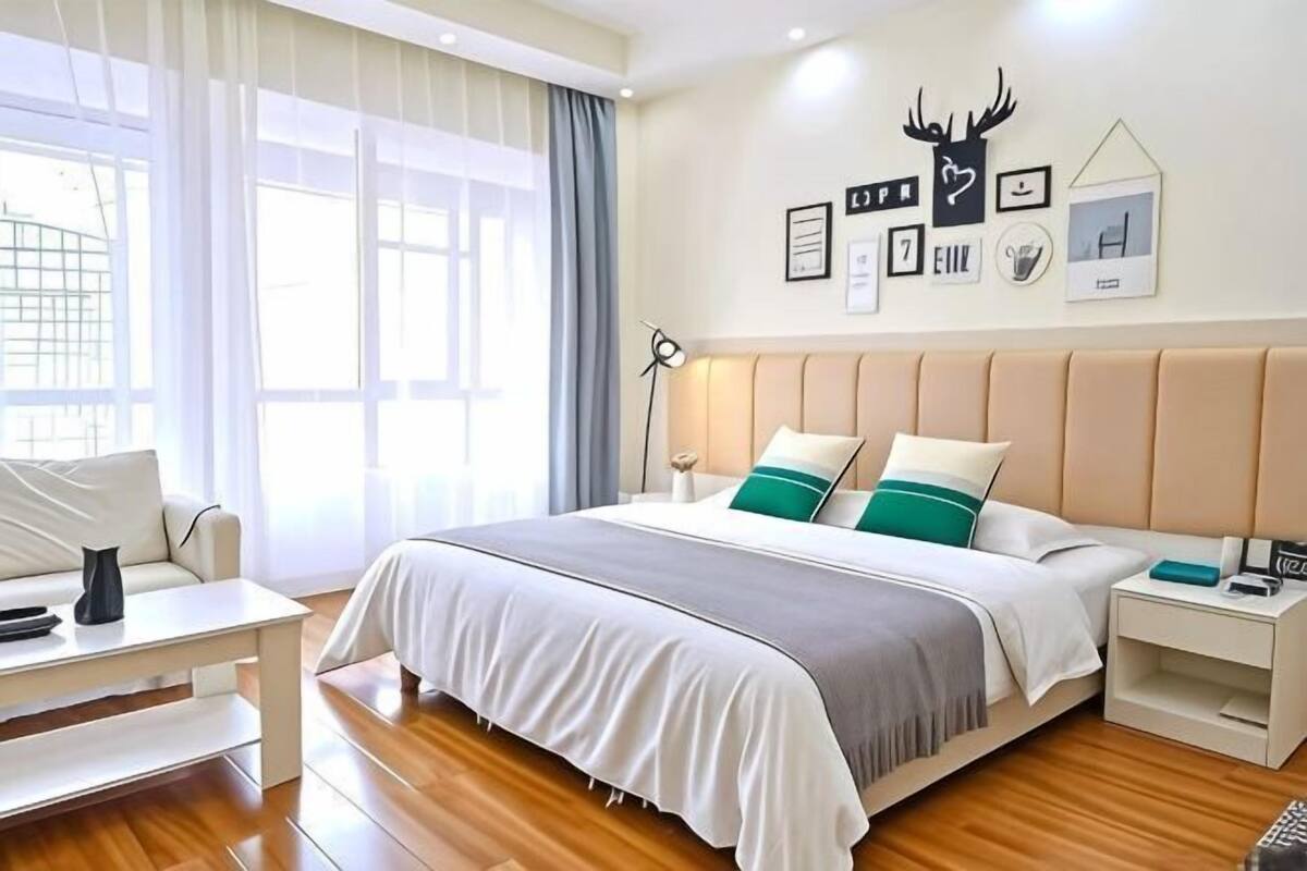 Una habitación de hotel con una cama, mesitas de noche, un escritorio y un ventanal grande.