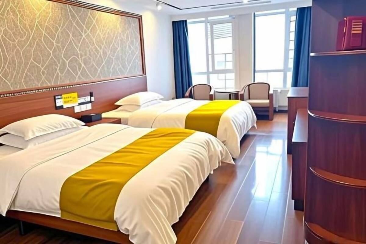 Habitación de hotel con dos camas, cabecera de madera, escritorio y estantería.