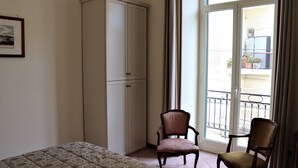 A bedroom with a bed, a wardrobe, two chairs, and a balcony with a railing. - Domus Marisa - Panoramic apartment in Naples area Posillipo/Mergellina (Napoli)