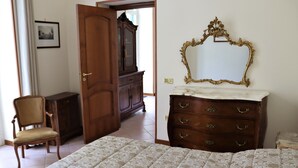 A bedroom with a bed, a wooden dresser, a chair, and a large mirror. - Domus Marisa - Panoramic apartment in Naples area Posillipo/Mergellina (Napoli)