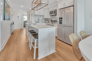 A modern kitchen with white cabinetry, stainless steel appliances, and a central island with bar stools.