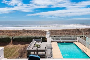 A pool area with a view of the beach, a lifeguard tower, and a sign indicating public access.