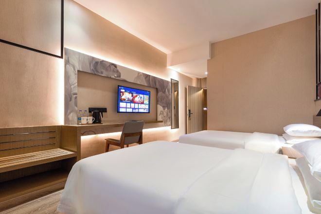 Ein Hotelzimmer mit zwei Betten, einem an der Wand montierten Fernseher, einer Holzbank und einem kleinen Tisch mit Kaffeemaschine.