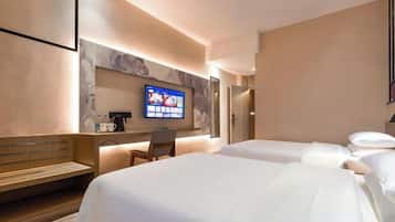 Ein Hotelzimmer mit zwei Betten, einem an der Wand montierten Fernseher, einer Holzbank und einem kleinen Tisch mit Kaffeemaschine.