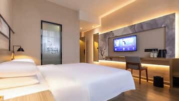 Ein modernes Hotelzimmer mit einem großen Bett, einem Schreibtisch mit Computer und einem Fernseher.