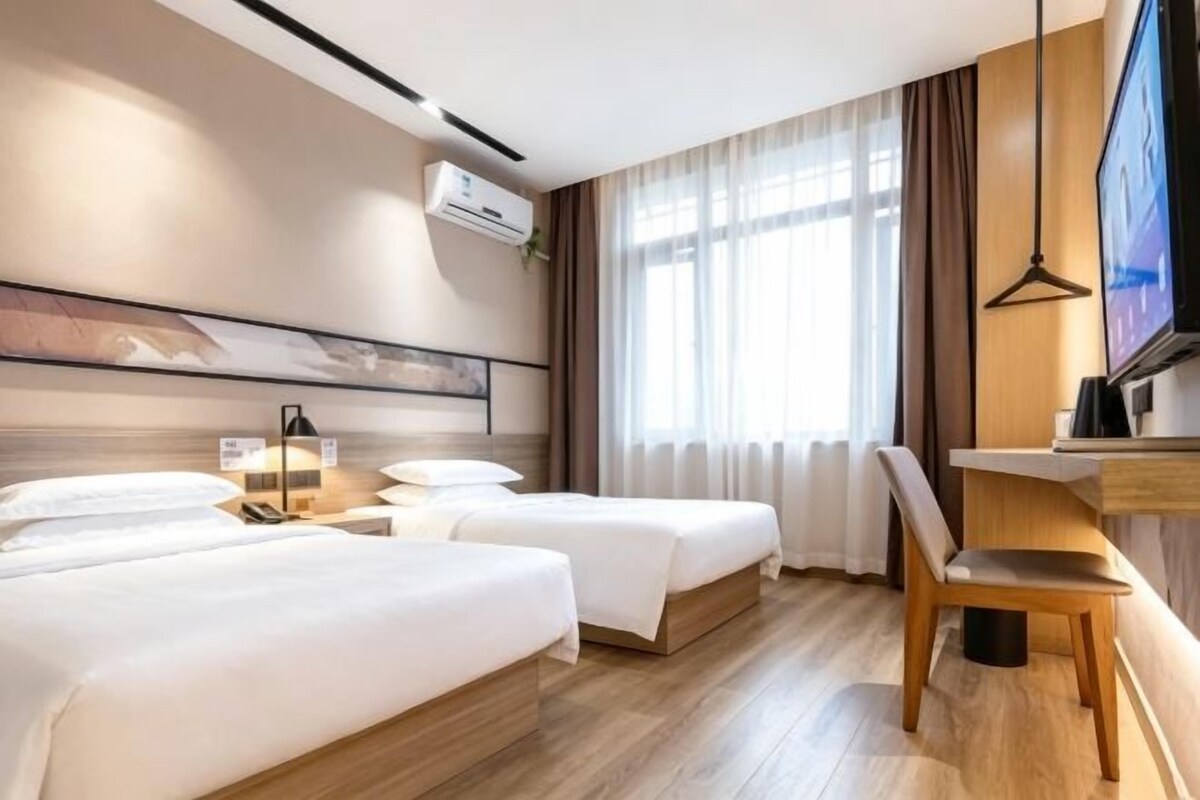 A hotel room with two beds, a desk, a chair, a television, and a window with curtains.