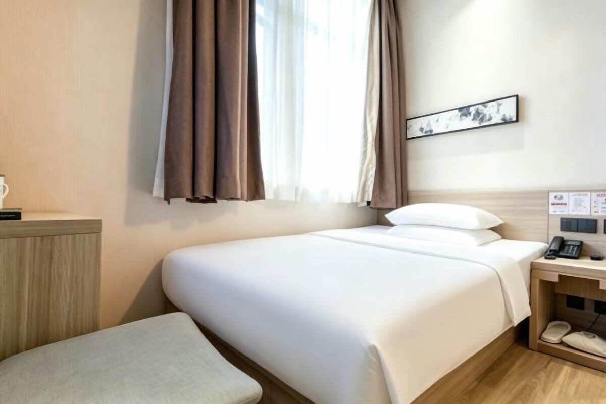 A hotel room with a bed, bedside table, and a small seating area.