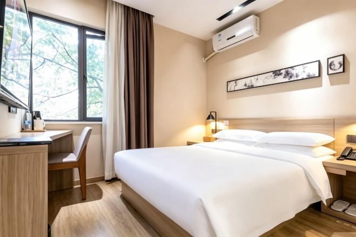 A hotel room with a bed, desk, chair, and window.