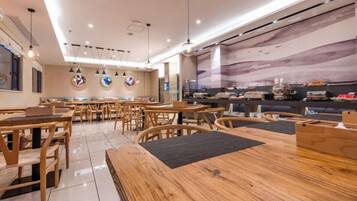 A modern restaurant interior with wooden tables and chairs, a counter with a menu, and a large mural on the wall.