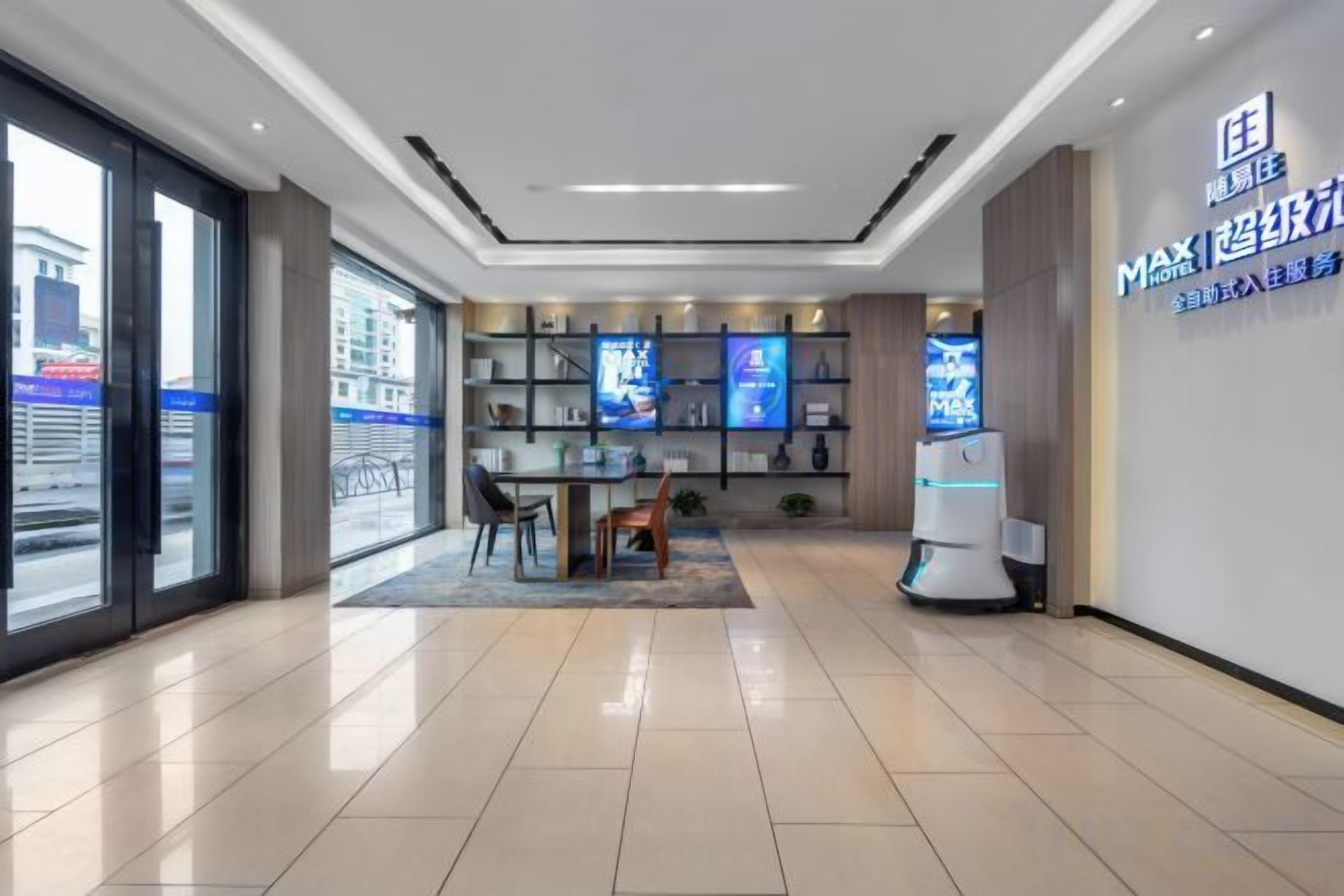 A modern hotel lobby with a reception desk, seating area, and a large digital display.