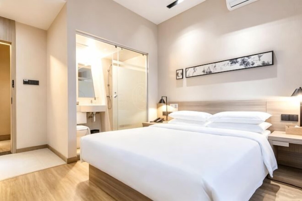 A hotel room with a large bed, a walk-in closet, and a bedside table with a lamp.