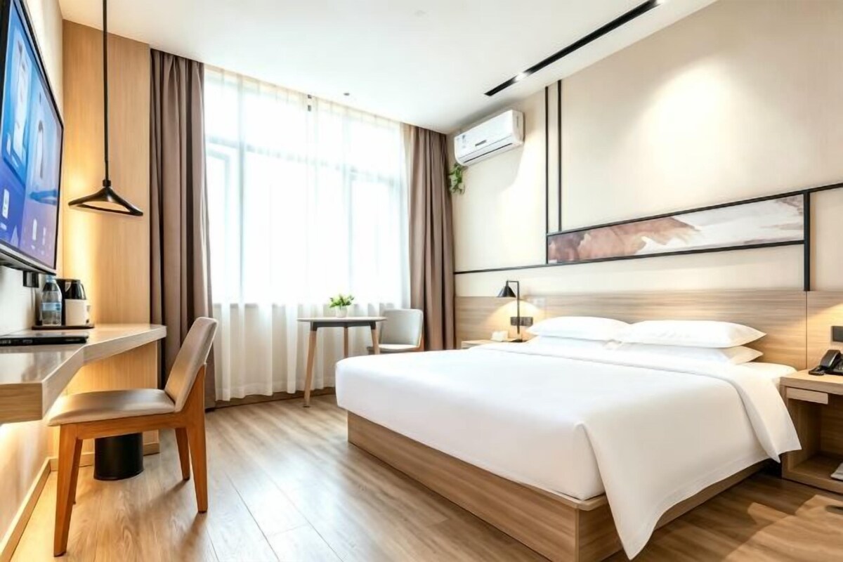 A modern hotel room with a bed, desk, chair, and a television.