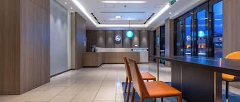 A modern hotel lobby with a reception desk, seating area, and large windows.