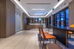 Een moderne hotellobby met een receptiebalie, een zithoek en grote ramen.
