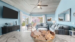 Una sala de estar moderna con una isla de mármol, ventilador de techo y un gran ventanal que da a un espacio exterior.