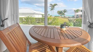 Una mesa y sillas de madera en una habitación con un ventanal que da a una playa y palmeras.
