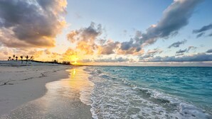 Una playa con un atardecer, cielo despejado y mar tranquilo.