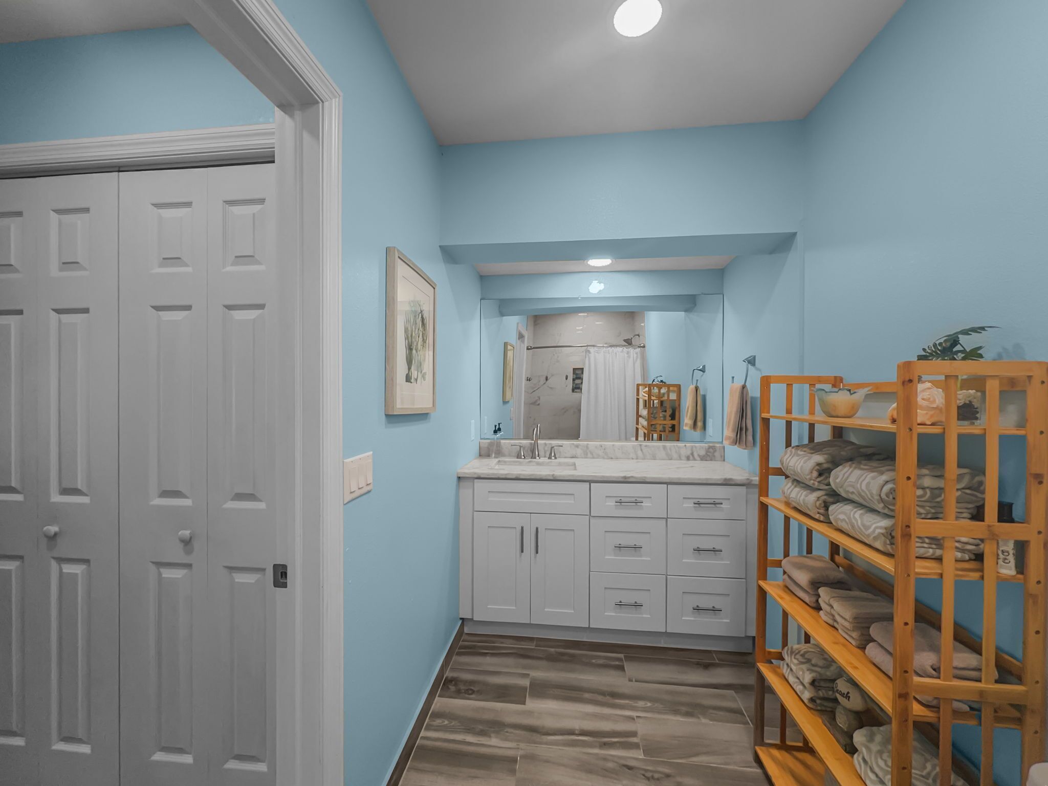 A hallway with a bathroom featuring a sink, mirror, and towel rack.