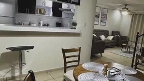 A modern kitchen with white and black cabinets, a bar stool, and a dining table with placemats. - Residencia Cálida y acogedora (Santa Tecla)