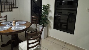 A dining area with a round table, chairs, a potted plant, and a clock on the wall. - Residencia Cálida y acogedora (Santa Tecla)