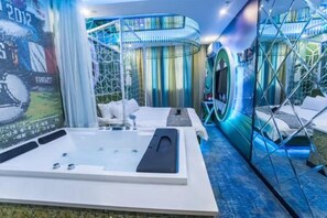 Un moderno spa con una bañera grande, una zona de estar con camilla de masaje y una pared con pantalla digital.