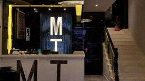 A reception desk with 'MT' illuminated letters, a staircase, and a potted plant. - Mt Theme Hotel Shanghai (Shanghai)