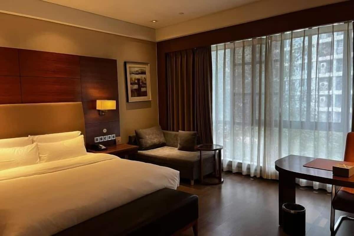 A hotel room with a large bed, a sofa, a small table, and a window with curtains.